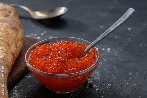 Red caviar in glass jar with silver spoon on the dark rustic background
