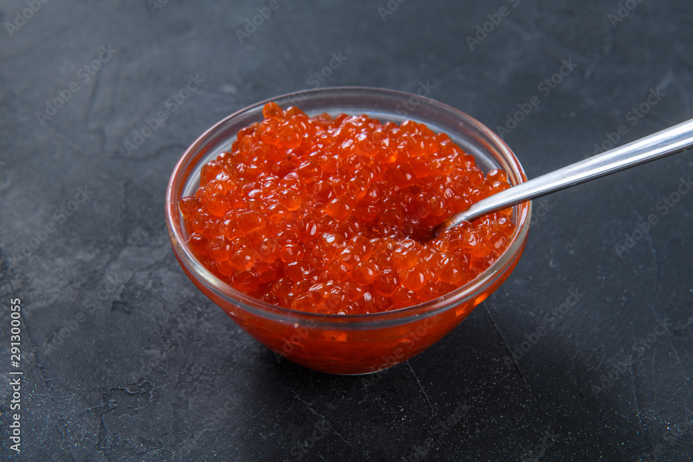 Red caviar in glass jar with silver spoon on the dark rustic background Red caviar in glass jar with silver spoon on the dark rustic background