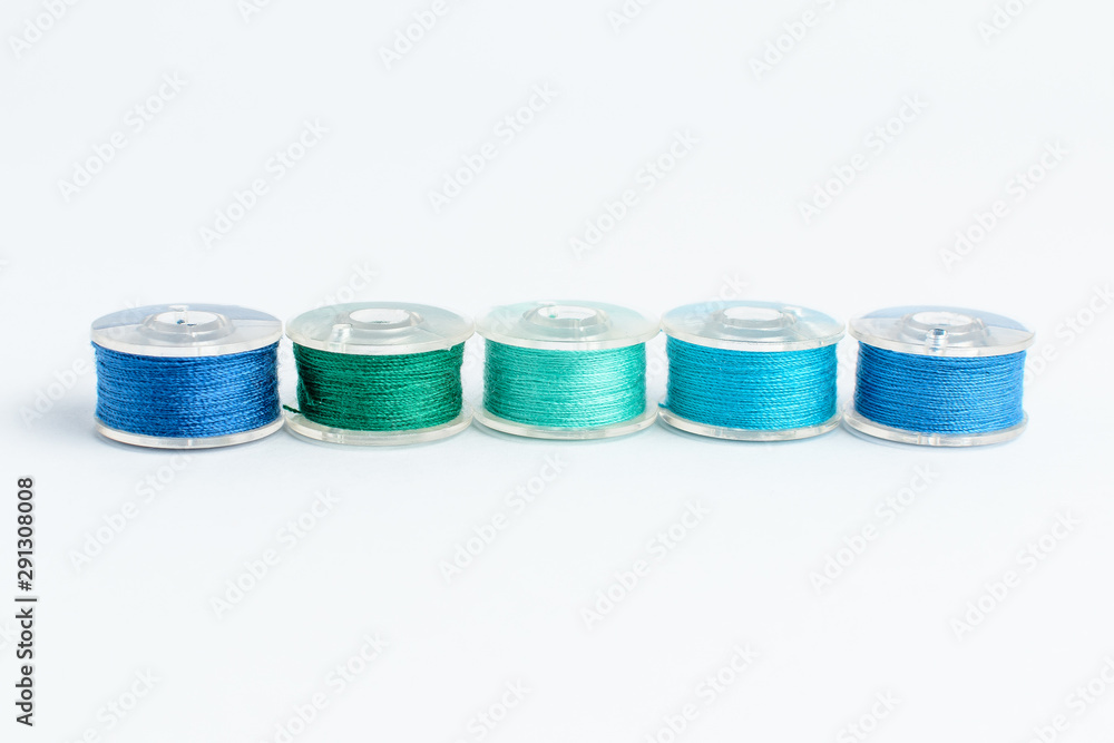 Five spools of blue and green mixed threads prepared for the sewing machine, isolated on white, side view Five spools of blue and green mixed threads prepared for the sewing machine, isolated on white, side view