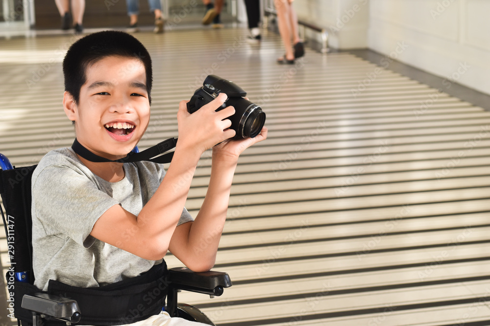 Photographer child on wheelchair is holding a camera in hand..He was smiling and having fun with it, Life in the education age of disabled children, Happy disabled kid concept.
