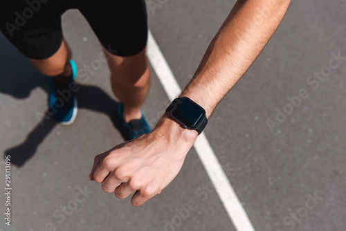 partial view of athletic young sportsman showing smartwatch with blank screen on running track