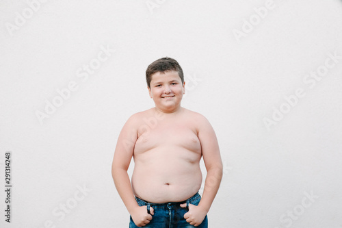 overweight concept of happy smiling fat little caucasian kid in jeans standing on bright wall background with copy space