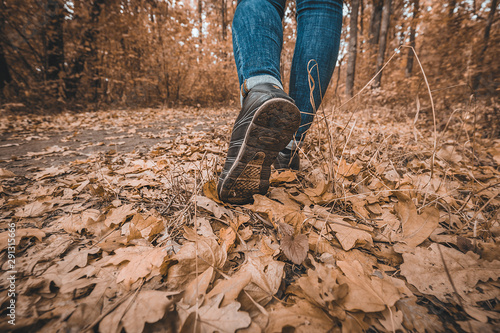 Young girl in jeans and sneakers on his feet, walks through the fall leaves on the road in the woods in the sunshine outdoors