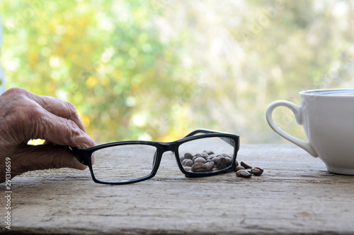 elderly woman hands holds glasses. Nearby is a cup of coffee. Garden terrace. Concept - morning breakfast, reading.