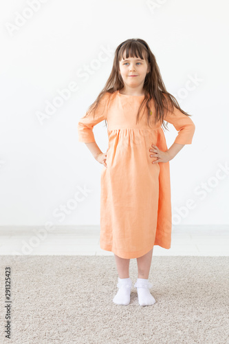 Pretty child girl posing for the camera, in a orange short dress, white background with copy space