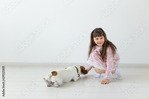 Little child girl in a pink dress plays with her dog Jack Russell Terrier