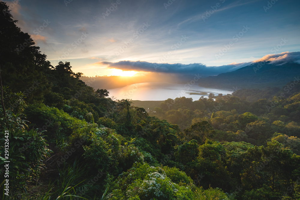 Beautiful Sunset over Lake Buyan Bali Indonesia. Island Coastal Scenery Nature Landscape. Amazing View on Green Bushes and Trees Forest Jungle Hill, Cloudy Sky and Sun. Shoreline from Climb