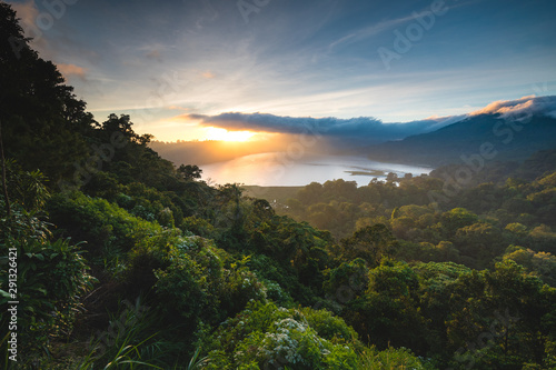 Beautiful Sunset over Lake Buyan Bali Indonesia. Island Coastal Scenery Nature Landscape. Amazing View on Green Bushes and Trees Forest Jungle Hill, Cloudy Sky and Sun. Shoreline from Climb