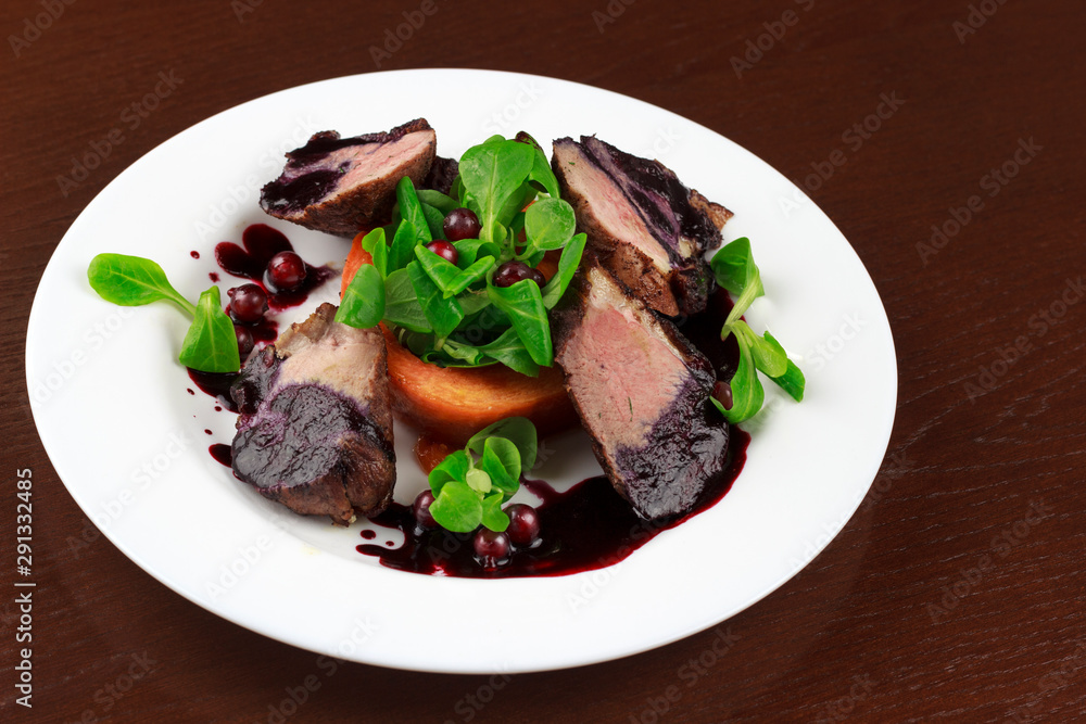 baked duck fillet in a sauce with herbs and berries in a plate