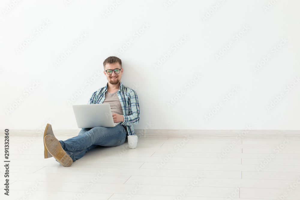 © satura_ - Positive young man in casual clothes surfing the Internet in search of new housing sitting on the floor in an empty room. The concept of finding an apartment using the Internet and a laptop. Copyspace © satura_ - Positive young man in casual clothes surfing the Internet in search of new housing sitting on the floor in an empty room. The concept of finding an apartment using the Internet and a laptop. Copyspace