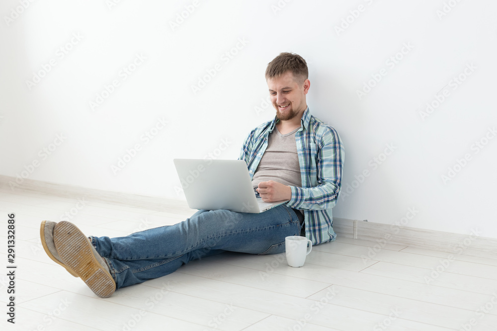 Positive young man in casual clothes and glasses surfing the Internet using Wi-Fi and a laptop in search of rental housing. Housewarming and apartment search concept. Positive young man in casual clothes and glasses surfing the Internet using Wi-Fi and a laptop in search of rental housing. Housewarming and apartment search concept.