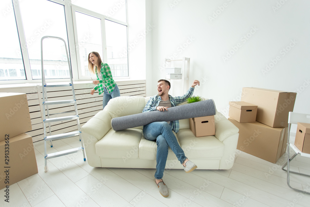 Positive crazy cheerful couple rejoices in moving their new apartment sitting in the living room with their belongings. Concept of housewarming and mortgages for a young family. Positive crazy cheerful couple rejoices in moving their new apartment sitting in the living room with their belongings. Concept of housewarming and mortgages for a young family.
