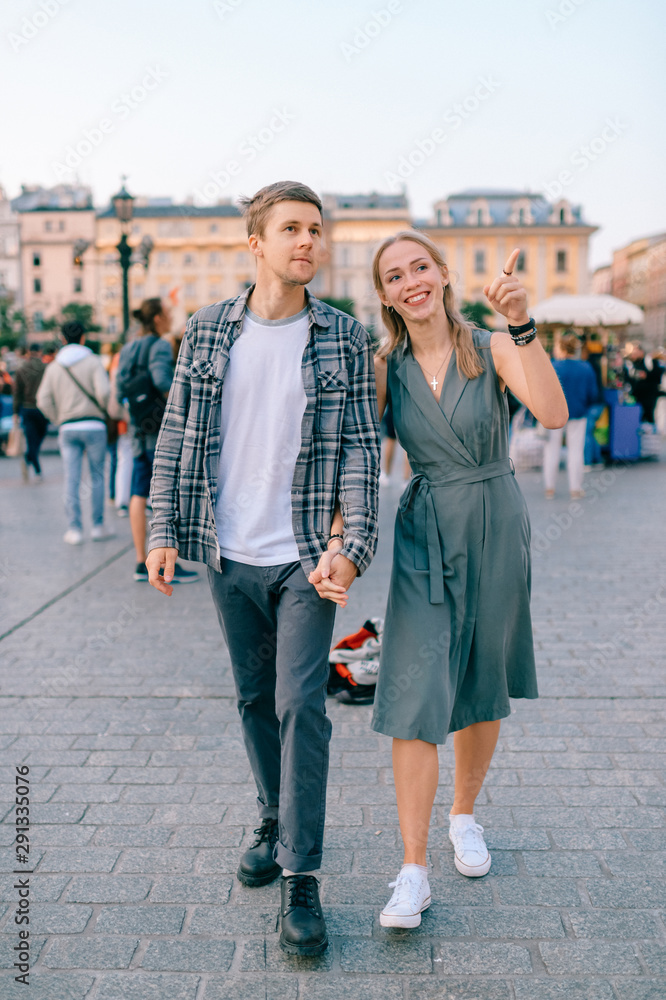 Happy loving couple smiling and walking throug the main square in Krakow (Cracow)
