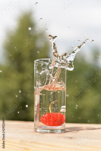 Ripe strawberries fell into a transparent glass of water and sprayed water around