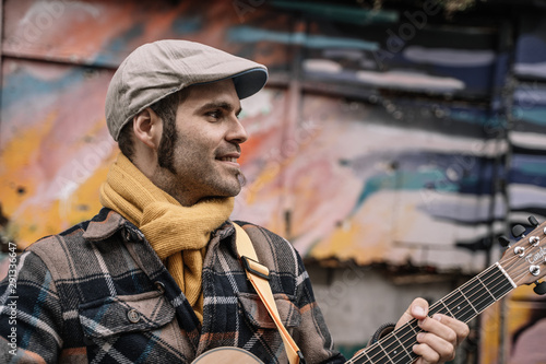 handsome man looking aside while is playing the guitar for a street performance