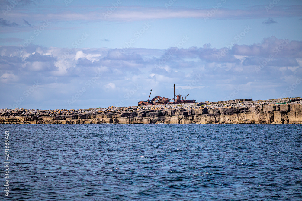 Beautiful view of the Plassey shipwreck on the rocky beach of  Inis Oirr island seen from a boat, wonderful sunny day with a blue sky and white clouds in the Aran Islands, Ireland