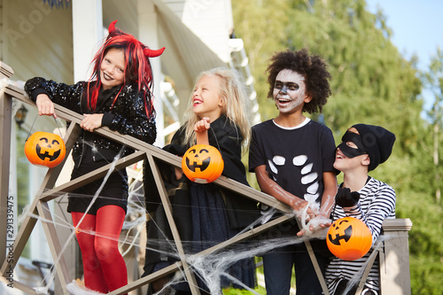 Multi-ethnic group of happy children posing on decorated porch while trick or treating together in Halloween season