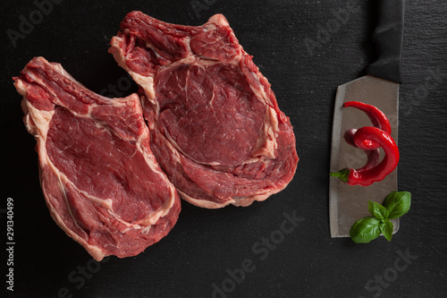 Raw fresh Beef steak with bone, spices and seasonings on stone cutting board. Top view, close upon black background photo