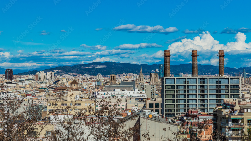 Beautiful aerial view of a part of the city of Barcelona Spain, distinguishing three chimneys on a wonderful and sunny day with a blue sky and white clouds on the horizon, travel concept