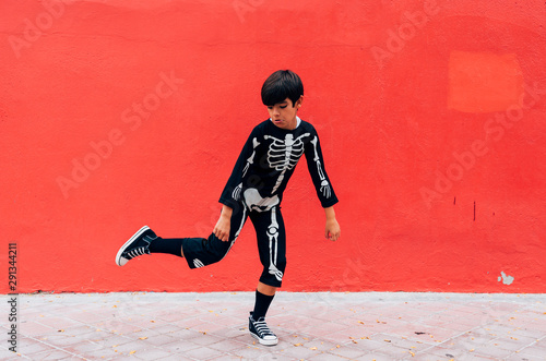 Boy in skeleton costume standing dancing in street on the red background