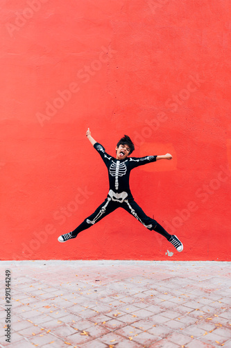 Boy in skeleton costume standing jumping in street on the red background