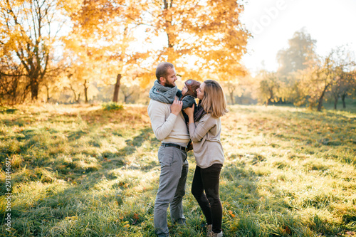 Happy family couple hugs their lovely baby in sunny autumn park. © benevolente