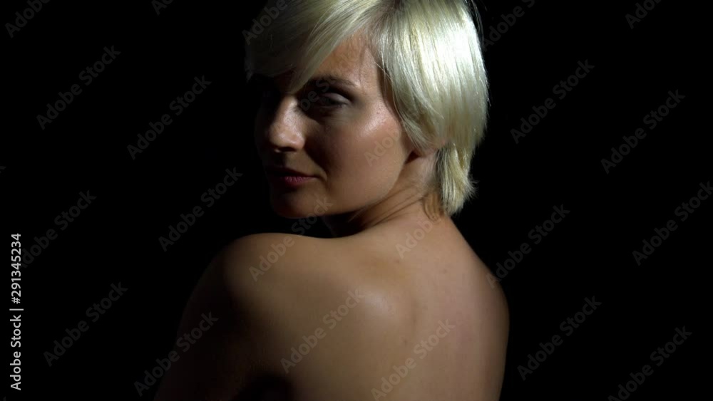 Naked blonde girl is posing sideways in the camera. Black background zoom out shot. Naked blonde girl is posing sideways in the camera. Black background zoom out shot.