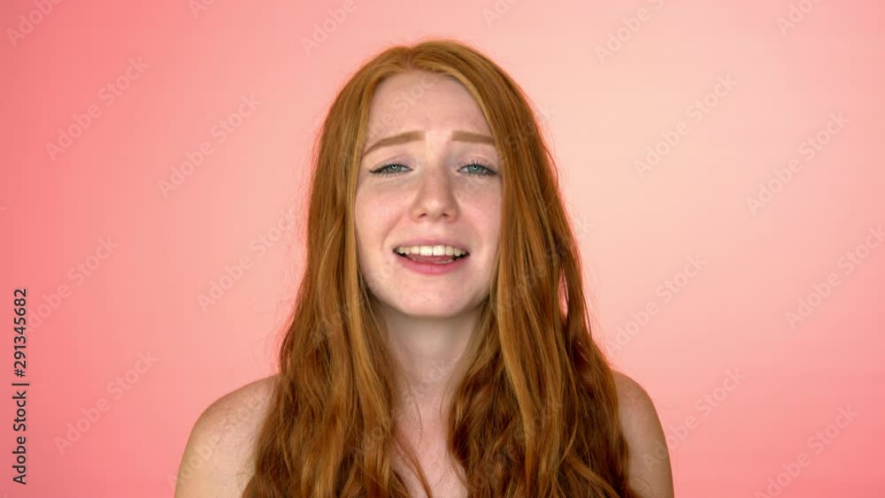 Slow motion shot of redhead female laughing into her hands in studio pink backdrop Slow motion shot of redhead female laughing into her hands in studio pink backdrop