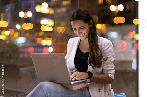 Young woman working on her laptop in the city at night