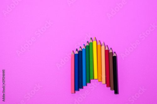 A variety of colored pencils are arranged in a beautiful pink background.