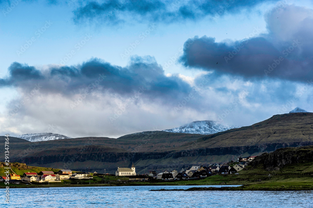 Evening view of little village with white church located in Faroe Islands.