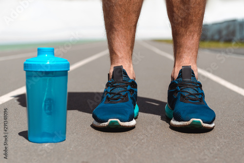 cropped view of young sportsman on running track near blue sports bottle