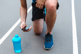 partial view of young sportsman on running track with blue sports bottle and smartphone