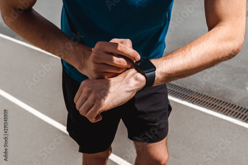 partial view of young sportsman using smartwatch on running track