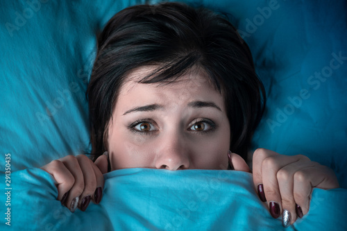 girl hides her face under the covers in bed. a nightmare after watching a horror movie. fear of nightmares photo