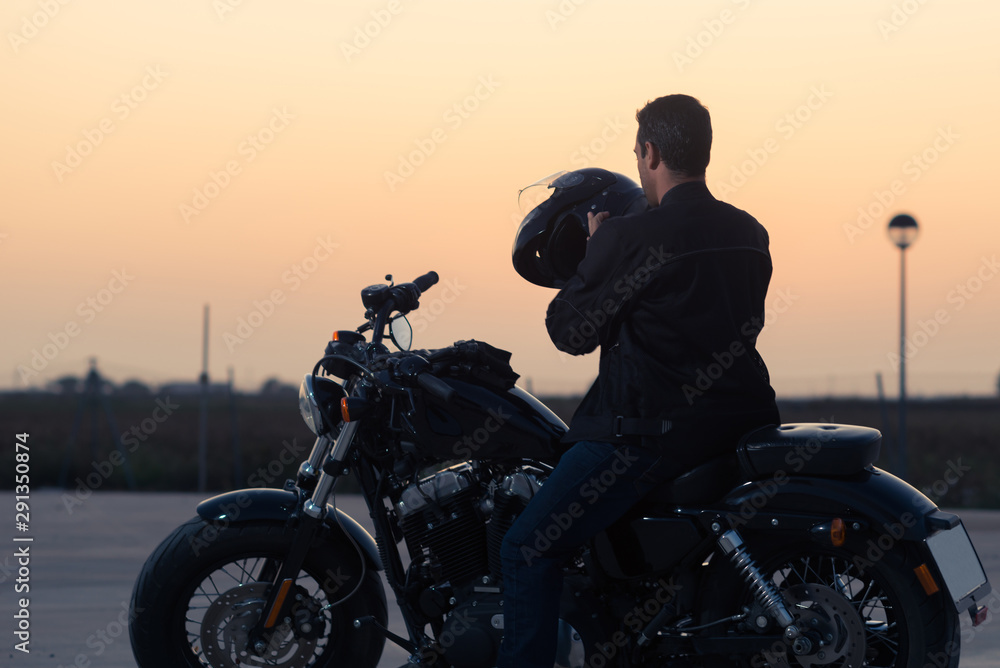 Fototapeta premium Black dressed biker man putting on a helmet.