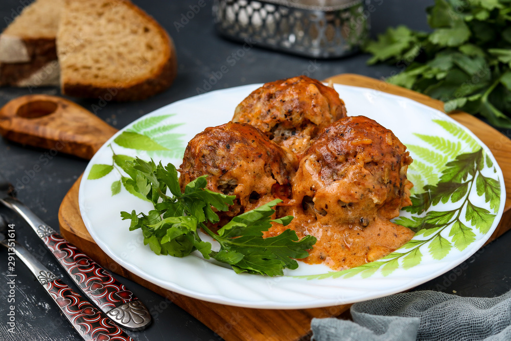 Meatballs in sour cream and tomatoes sauce in white plate against a wooden board, horizontal orientation Meatballs in sour cream and tomatoes sauce in white plate against a wooden board, horizontal orientation