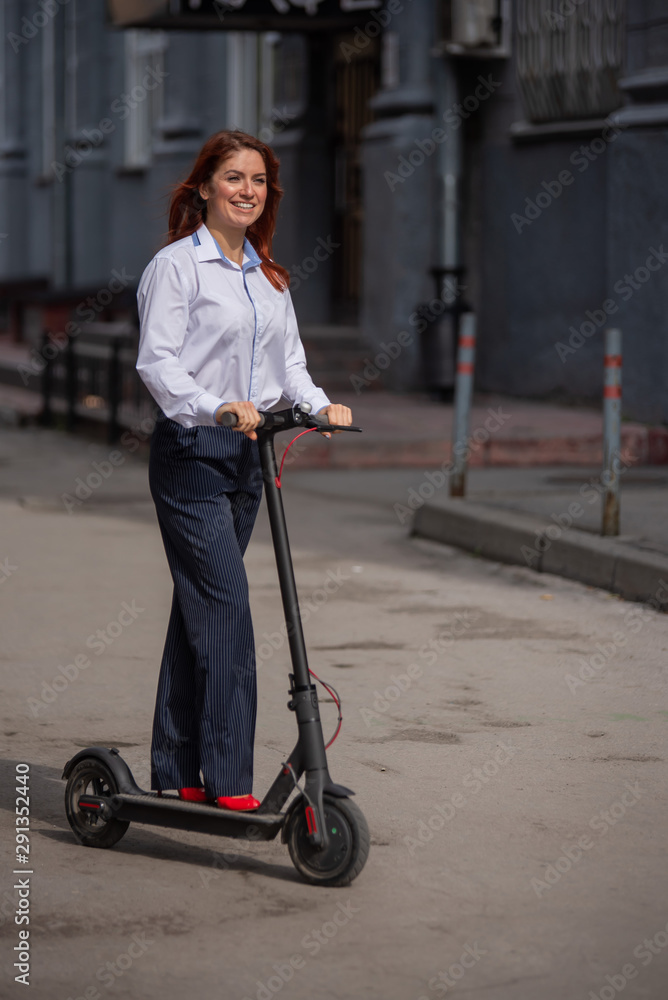 A red-haired girl in a white shirt drives an electric scooter along the wall. A business woman in a trouser suit and red high heels rides around the city in a modern car. dress code in the office. A red-haired girl in a white shirt drives an electric scooter along the wall. A business woman in a trouser suit and red high heels rides around the city in a modern car. dress code in the office.