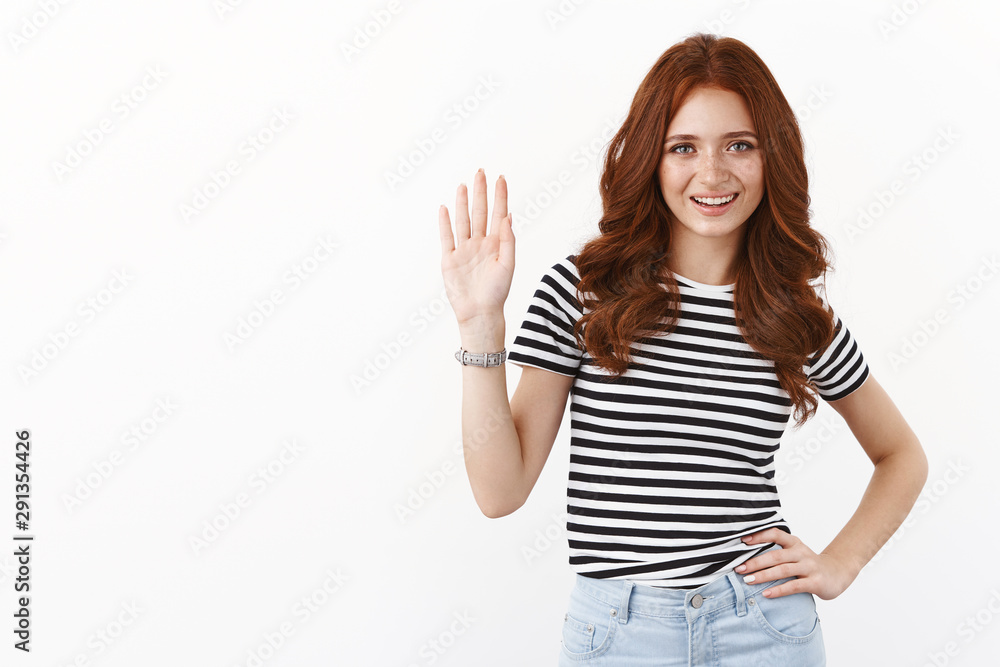 Cute friendly and casual young redhead caucasian girl in striped t-shirt, waving raised hand in greeting gesture, smiling joyfully, welcome friend, invite guest, saying hello or hi, white background Cute friendly and casual young redhead caucasian girl in striped t-shirt, waving raised hand in greeting gesture, smiling joyfully, welcome friend, invite guest, saying hello or hi, white background