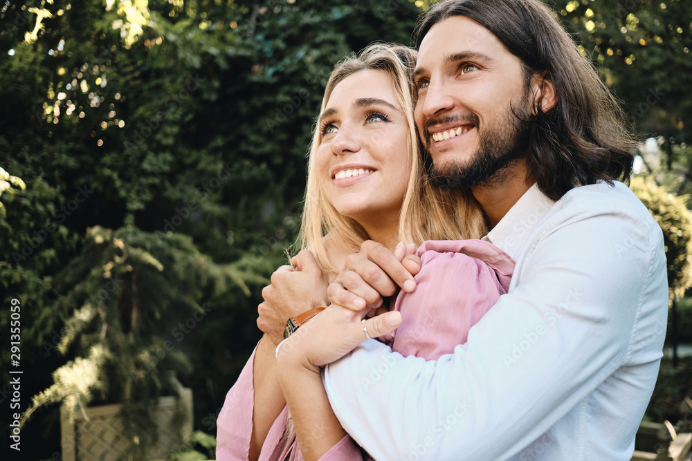 Fototapeta premium Young beautiful romantic couple hugging each other while happily looking away on date outdoor
