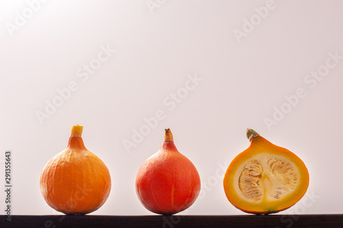 Tableau sur toile One red pumpkin, one yellow and one cut with seeds inside, lie in a row against a white background