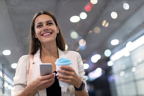 Young woman with smartphone and coffee in the city at night 