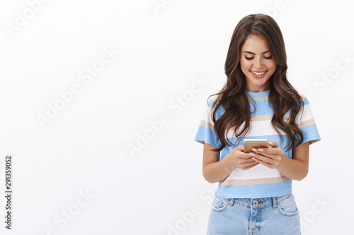 Lovely modern caucasian woman texting friend, hold smartphone, use mobile phone, browsing internet, watching funny video, scroll photo album and smiling while look device screen, white background