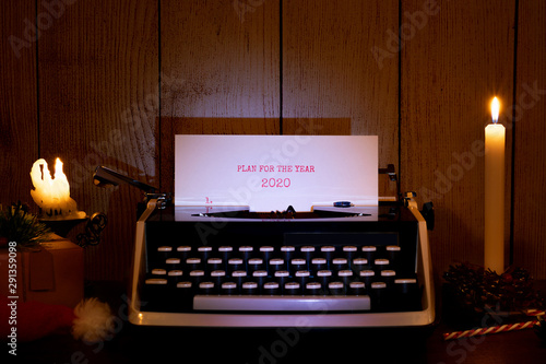 Old typewriter, a sheet of paper with the inscription "Plan for the year 2020". Dark Christmas and New Year background, with gifts and candles.