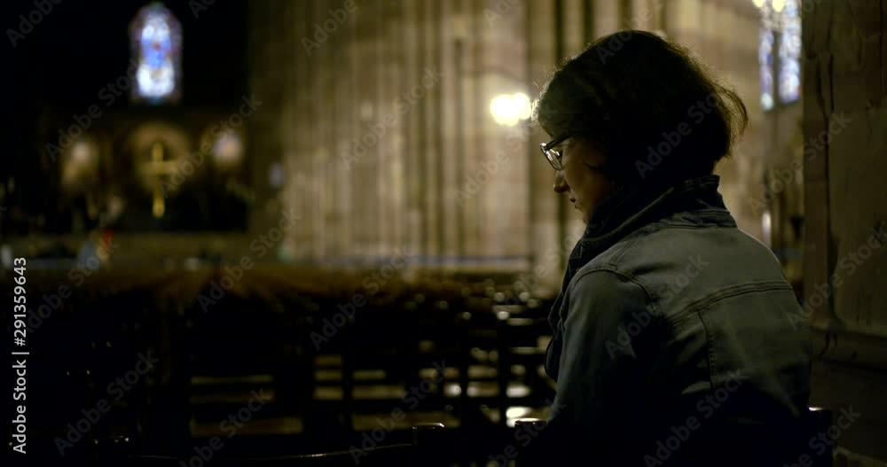 Portrait dark-haired woman of middle age, on her face she has glasses, she sits in a Catholic Cathedral on chairs. Rear view. Portrait dark-haired woman of middle age, on her face she has glasses, she sits in a Catholic Cathedral on chairs. Rear view.