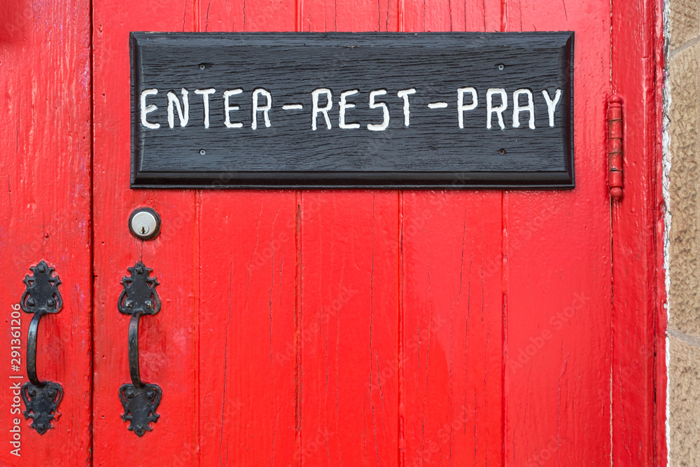 Black sign on bright red door inviting viewers to rest and pray in a small rural town Black sign on bright red door inviting viewers to rest and pray in a small rural town