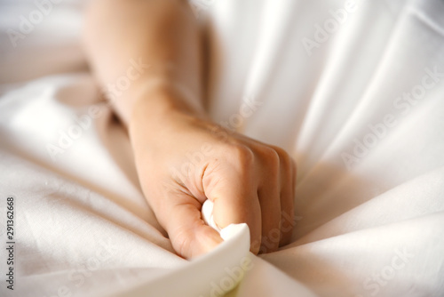 Female hand squeezes the sheet, symbolizes pleasure and orgasm