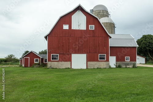 Multistory red barn with silos on green grass with an overcast sky