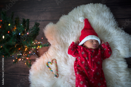 Little baby in red  cap of Santa Claus celebrates Christmas. Christmas  photo of infant newborn in red cap. New Year's holidays and Christmas tree. Little Santa