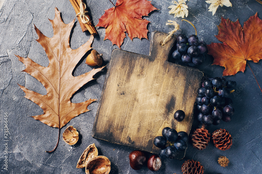 Autumn composition with cutting wooden board, marple leaves, freshly harvested ripe grapes, cones and wallnuts on dark stone table Autumn composition with cutting wooden board, marple leaves, freshly harvested ripe grapes, cones and wallnuts on dark stone table